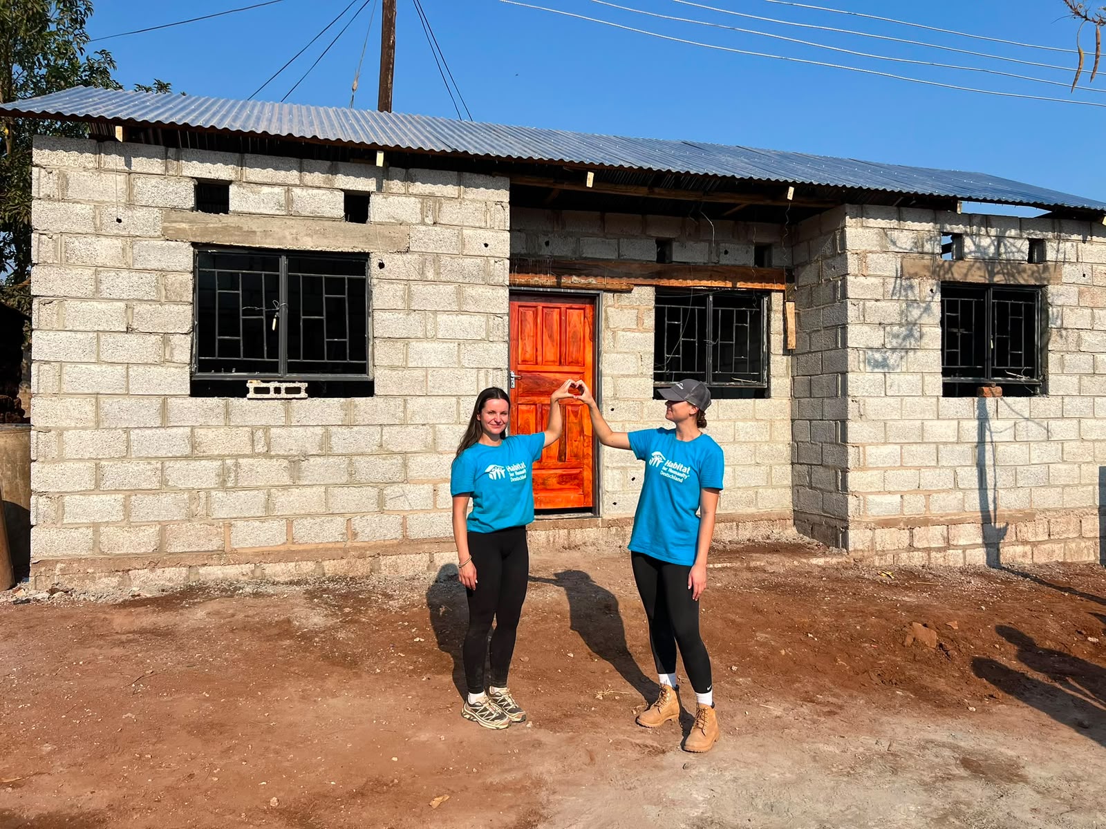 Immobilienberaterinnen Emilia Steiniger und Emilia Zyla mit dem fertigen Haus auf der Baustelle des HoffnunsBAUer-Freiwilligeneinsatzes in Sambia 2026