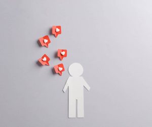 Papiermännchen auf grauem Hintergrund mit roten Social-Media-Sprechblasen und Herzen darüber