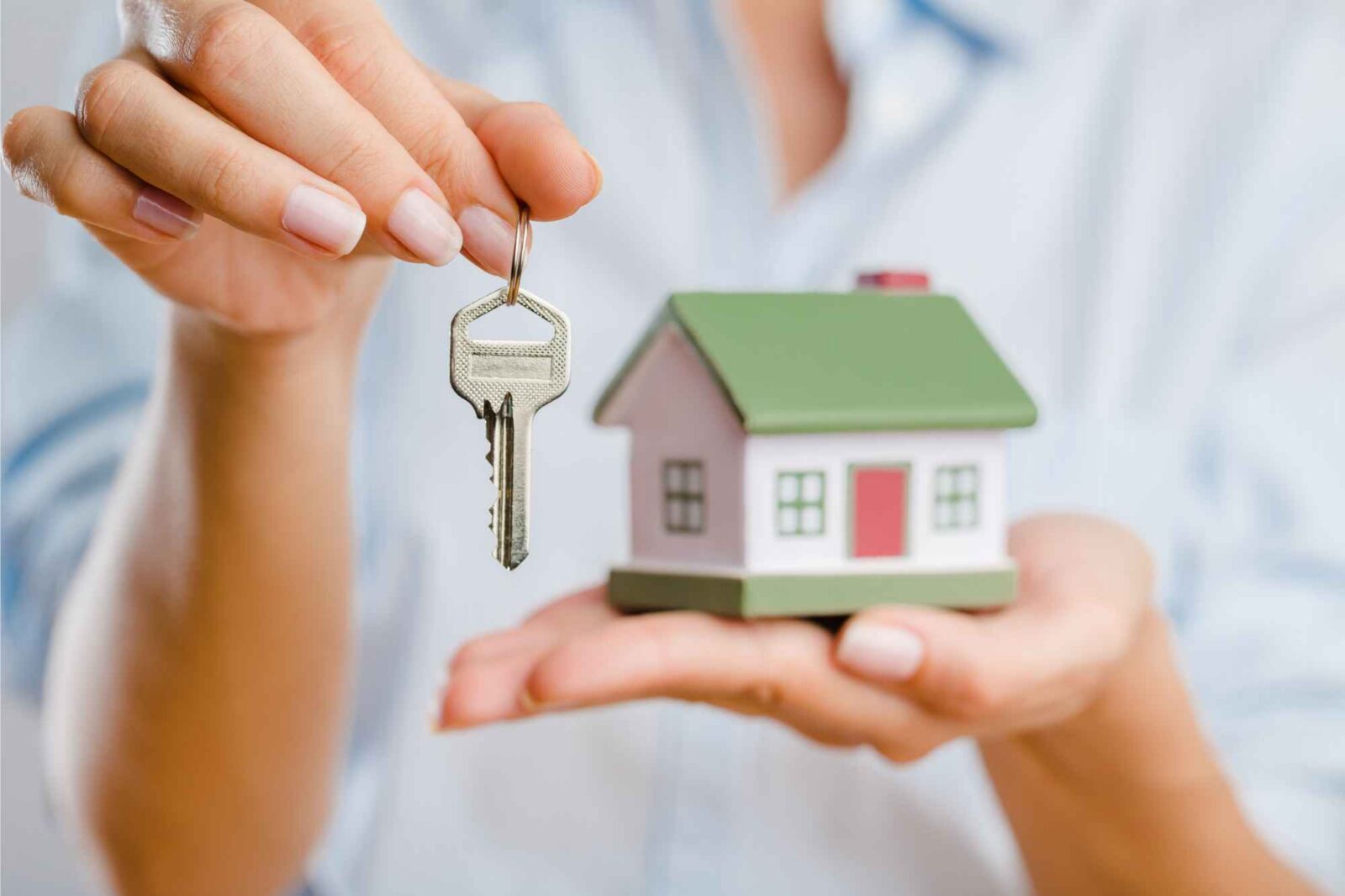 Frau hält kleines Haus in einer Hand und Schlüssel in der anderen