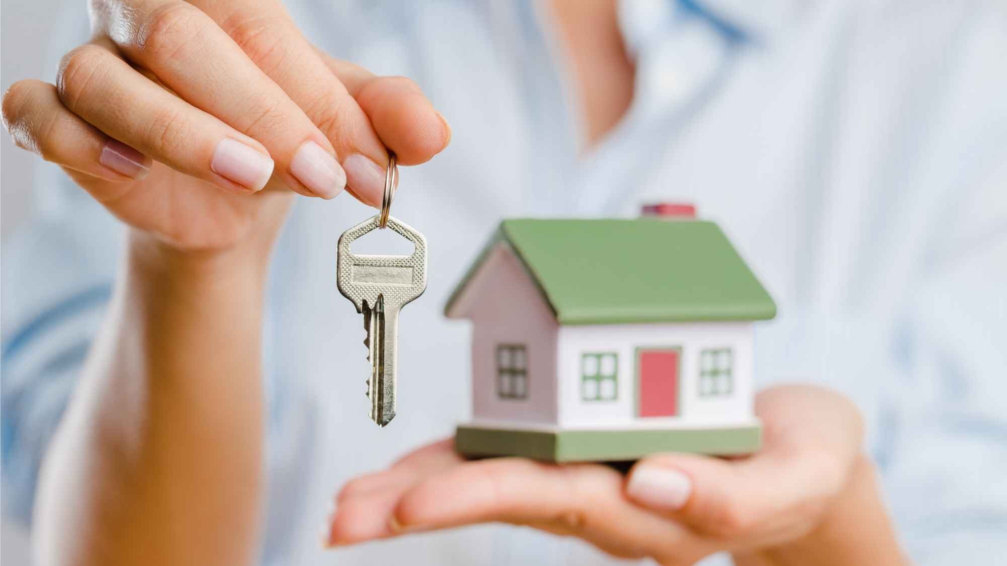 Frau hält kleines Haus in einer Hand und Schlüssel in der anderen