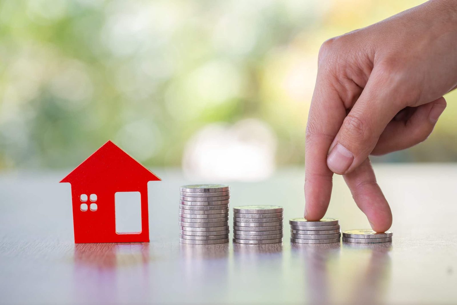 Spekulationssteuer bei Immobilien: Rotes Papierhaus neben Münzstapeln