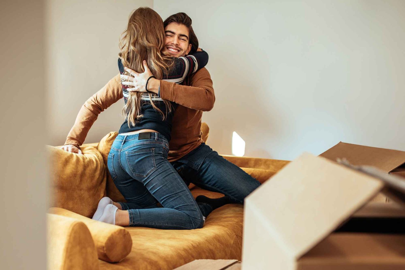 Pärchen umarmt sich auf Sofa, umgeben von Umzugskartons