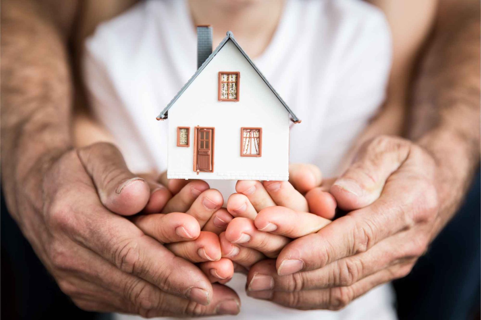 Alte und junge Hände halten gemeinsam Spielzeughaus