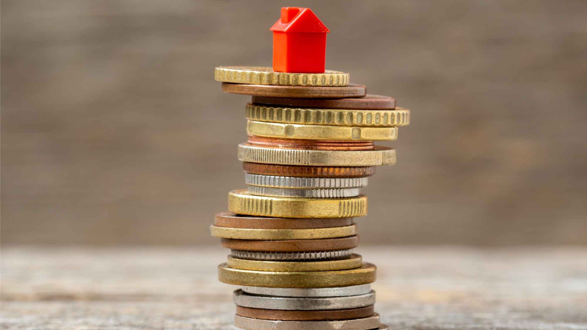 Rotes Spielzeughaus auf Stapel Geldmünzen