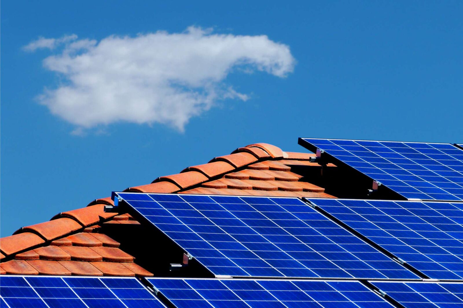 PV-Anlage auf rotem Häuserdach mit blauem Himmel und Wolke im Hintergrund