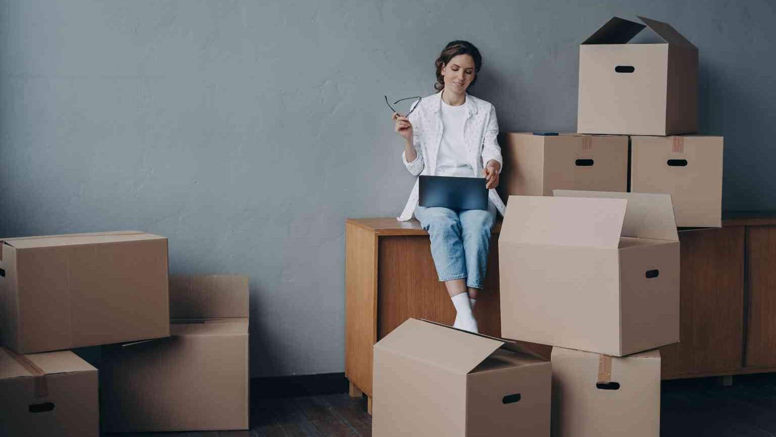Vermieterin sucht Mieter am Laptop, umgeben von Umzugskartons