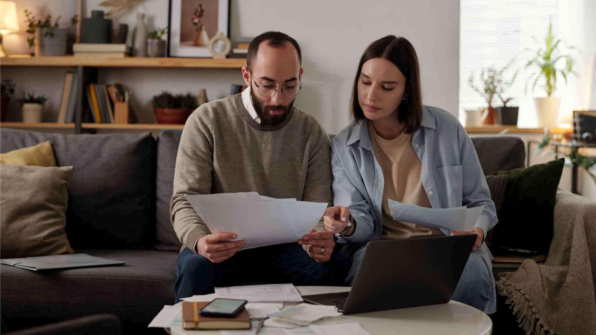 Paar sitzt mit einem Stapel Dokumenten auf dem Sofa und berechnet die Nebenkosten als Vermieter