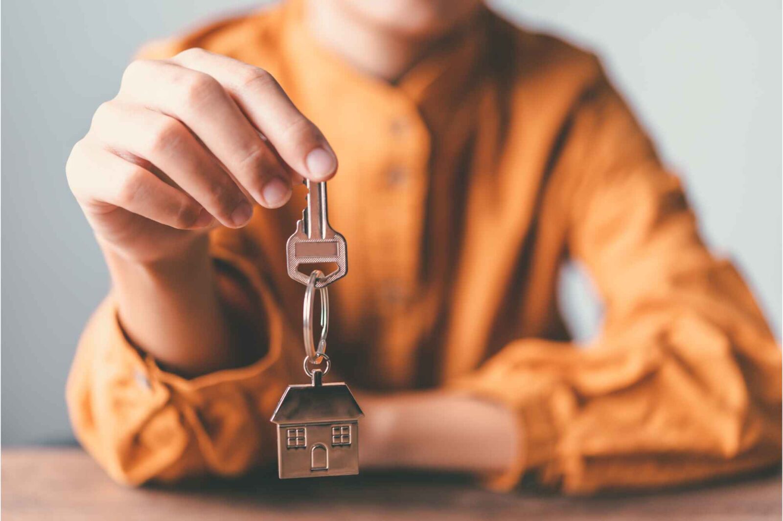 Frau in oranger Bluse hält Wohnungsschlüssel in der Hand.