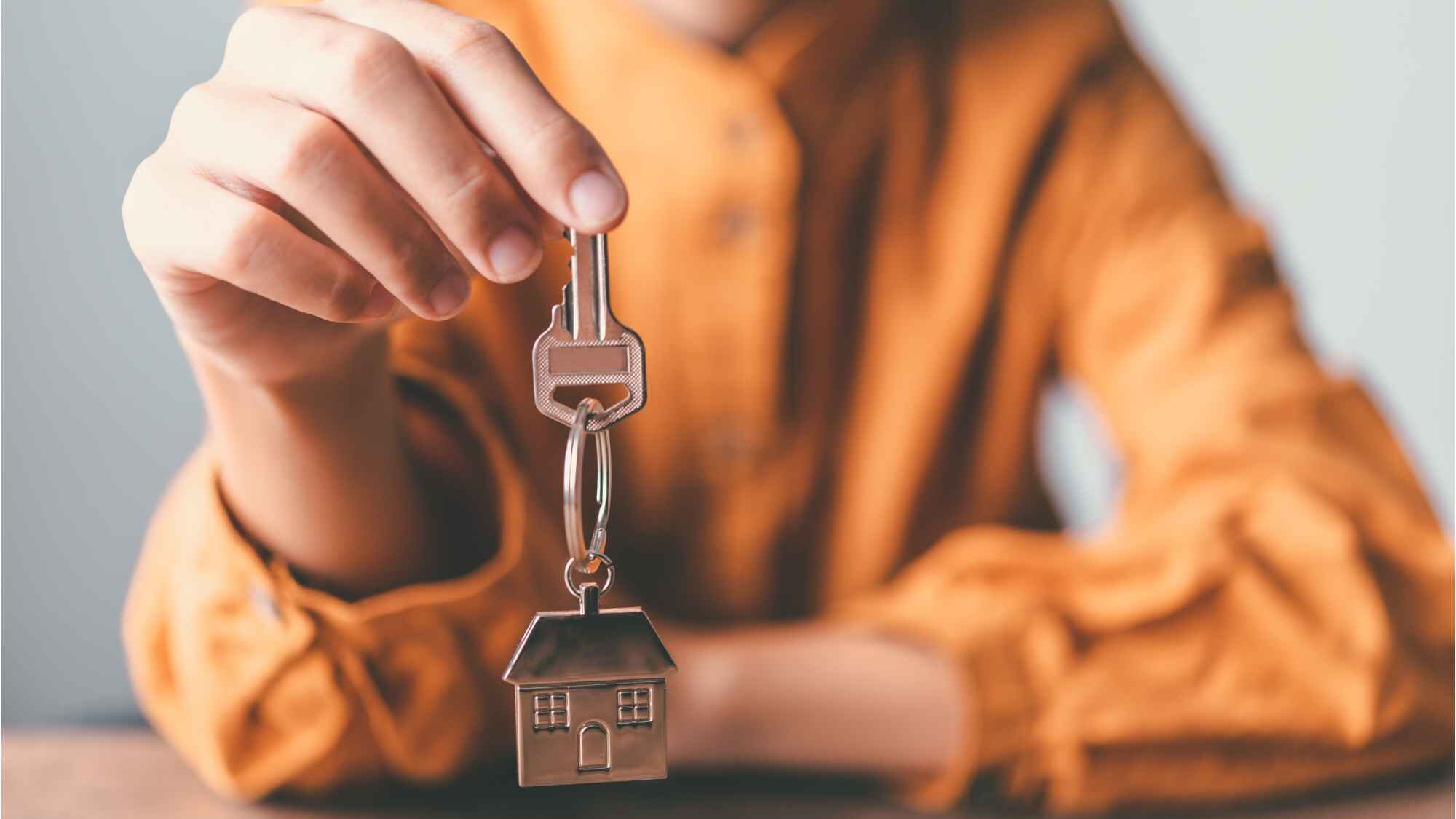 Frau in oranger Bluse hält Wohnungsschlüssel in der Hand.