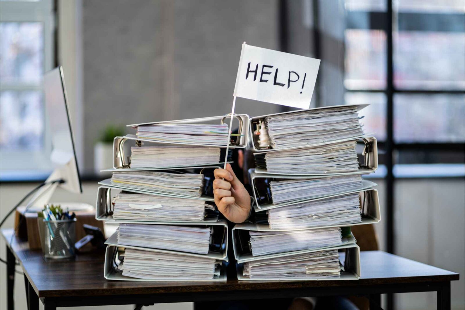 Mann zwischen Aktenordnern hält Fahne mit Aufschrift "Help" hoch