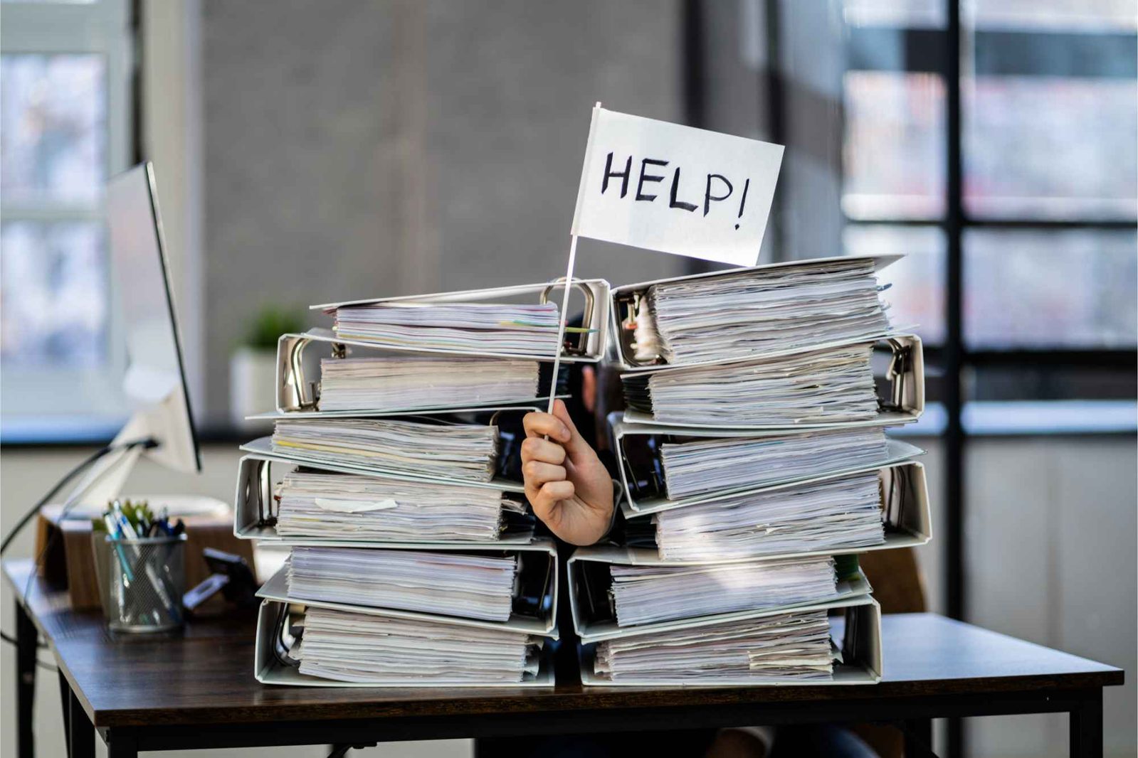 Mann zwischen Aktenordnern hält Fahne mit Aufschrift "Help" hoch