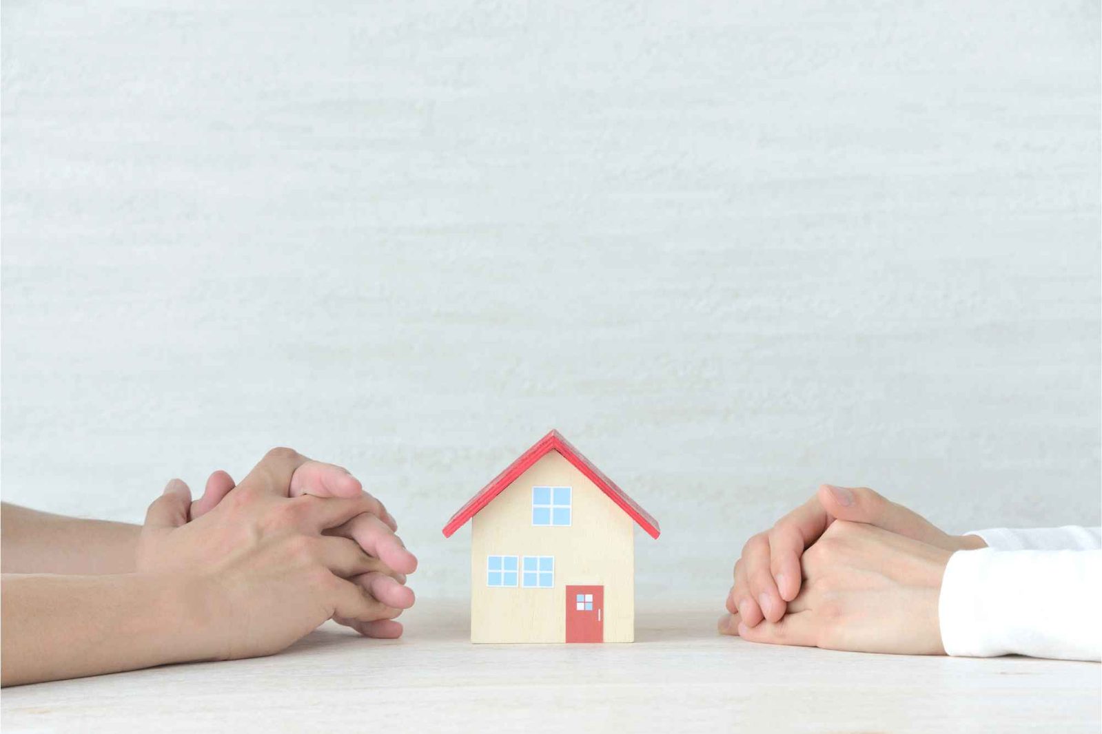 Zwei Personen sitzen sich gegenüber, Spielzeughaus steht zwischen ihren Händen auf dem Tisch