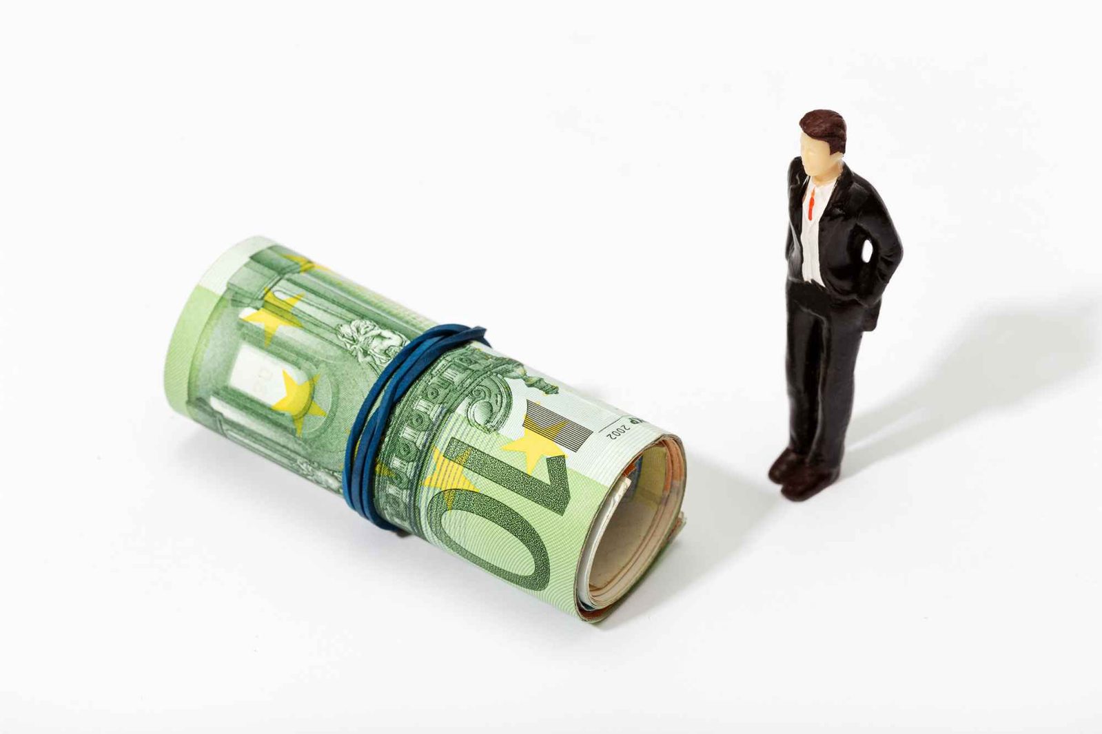 Miniaturmann mit roter Krawatte steht neben Rolle von Euroscheinen