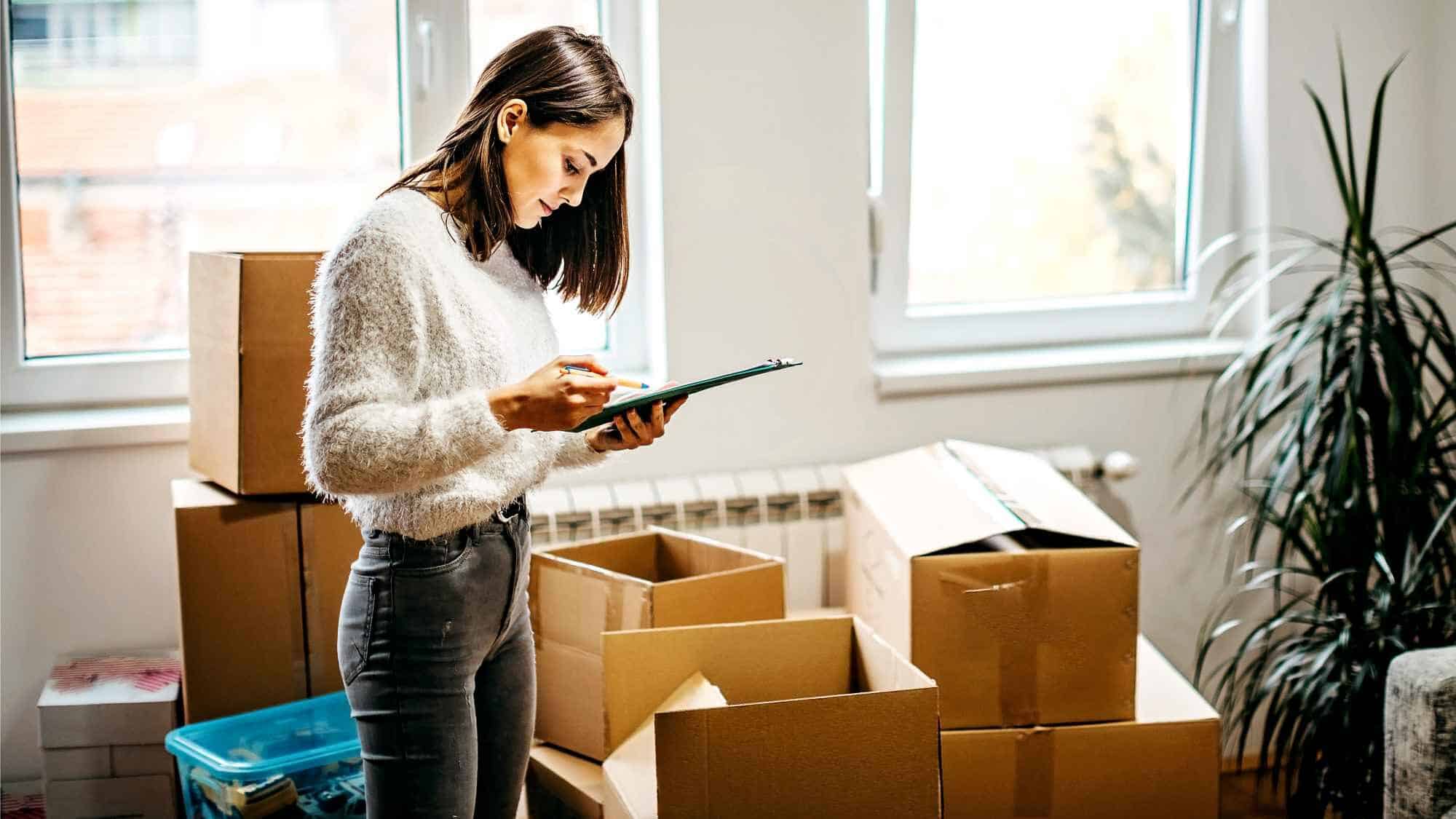 Frau mit Checkliste mit in Wohnung mit Umzugskartons im Hintergrund